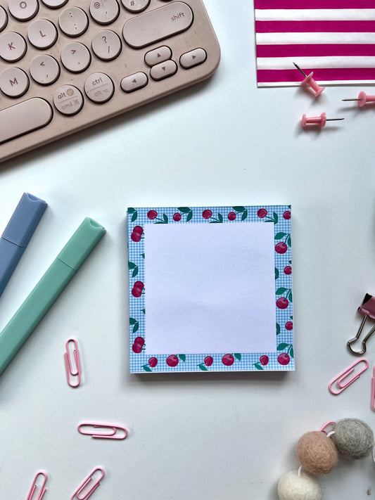 Small square memo block notepad with a blue plaid and cherry border on a desk with stationery items.