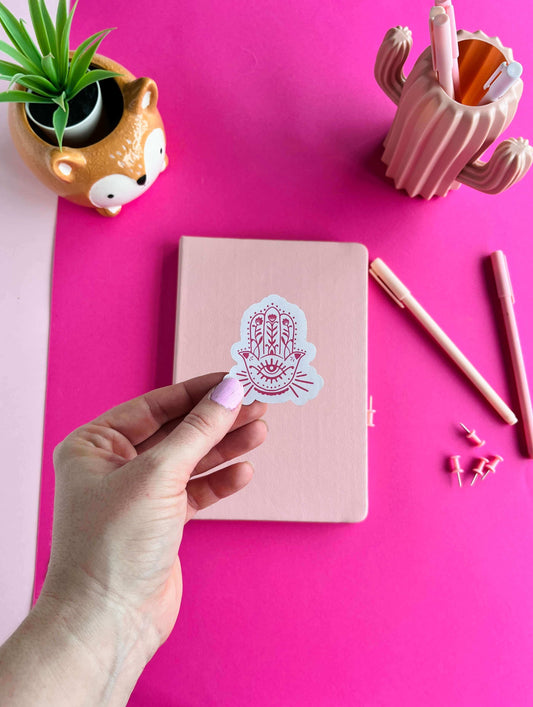 Hand holding a pink sticker of spiritual hamsa symbol